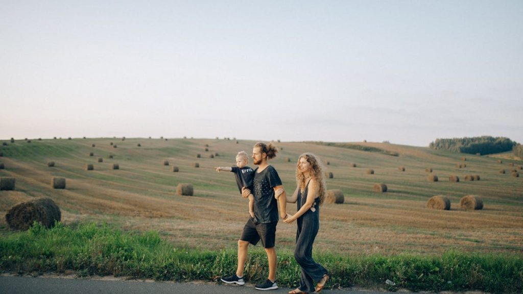 A joyful family walking hand in hand across a picturesque hayfield landscape at sunset.